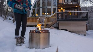 A cabin with a large glass front, wooden deck, and a fire pit in the snow. - "The Arched Chalet" Stunning Green Mountain views close to Killington and Okemo (Plymouth)