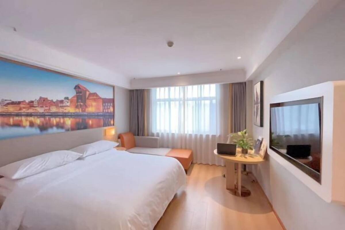 Una habitación de hotel con una cama grande, un escritorio con una computadora portátil, un cuadro de un paisaje urbano y un televisor en la pared.
