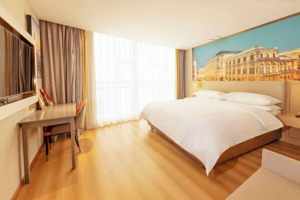 Habitación de hotel con una cama grande, un escritorio y un cuadro de un edificio en la pared.