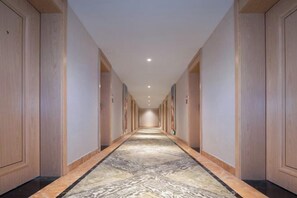 Corredor de hotel com carpete estampado, portas de madeira e iluminação embutida.