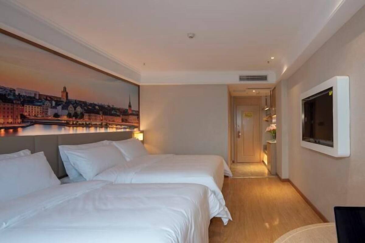 Habitación de hotel con dos camas, un cuadro de un paisaje urbano, un televisor y un pasillo que lleva a un baño.