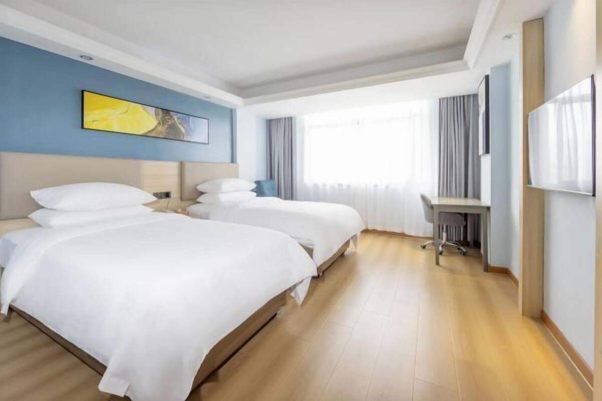 Una habitación de hotel con dos camas, un escritorio y un ventanal grande.