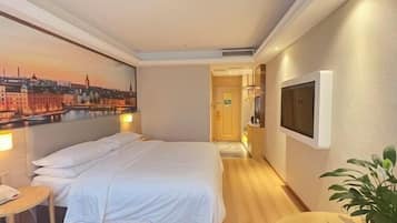 A hotel room with a bed, a TV, a painting of a cityscape, and a plant.