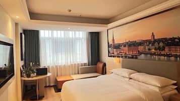 Habitación de hotel con una cama grande, un escritorio con una computadora portátil, un espacio de descanso y un cuadro de un paisaje urbano en la pared.