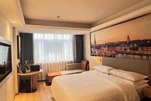 A hotel room with a large bed, a desk with a laptop, a seating area, and a cityscape painting on the wall. - Vienna Classic Hotel (Hengdian Film and Television City Dream Valley) (Dongyang)