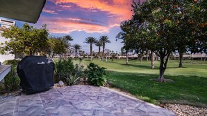 A patio with a grill, a well-maintained lawn, and a golf course in the background.