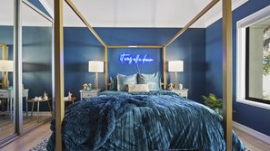 Une chambre à coucher avec un lit à baldaquin, un néon mural et une table de chevet avec une lampe.
