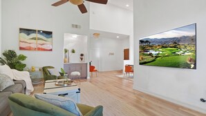 A spacious living room with a large flat-screen TV, comfortable seating, and a view of a golf course.