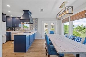 Une cuisine moderne avec des meubles de couleur bleu foncé, un îlot central et un coin repas comprenant une longue table et des chaises bleues.
