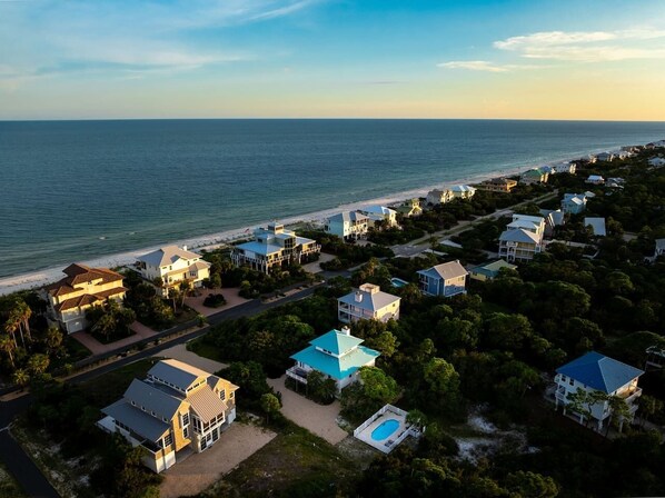 An aerial view of a coastal residential area with houses, a beach, and a clear sky.