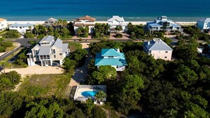 An aerial view of a coastal residential area with houses, a swimming pool, and a beach.