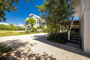 A two-story house with a gravel driveway, surrounded by trees and greenery.