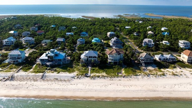 An aerial view of a coastal residential area with houses, a beach, and a view of the ocean.