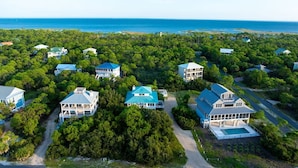 An aerial view of a coastal residential area with multiple houses, a clear view of the ocean, and a well-maintained landscape.