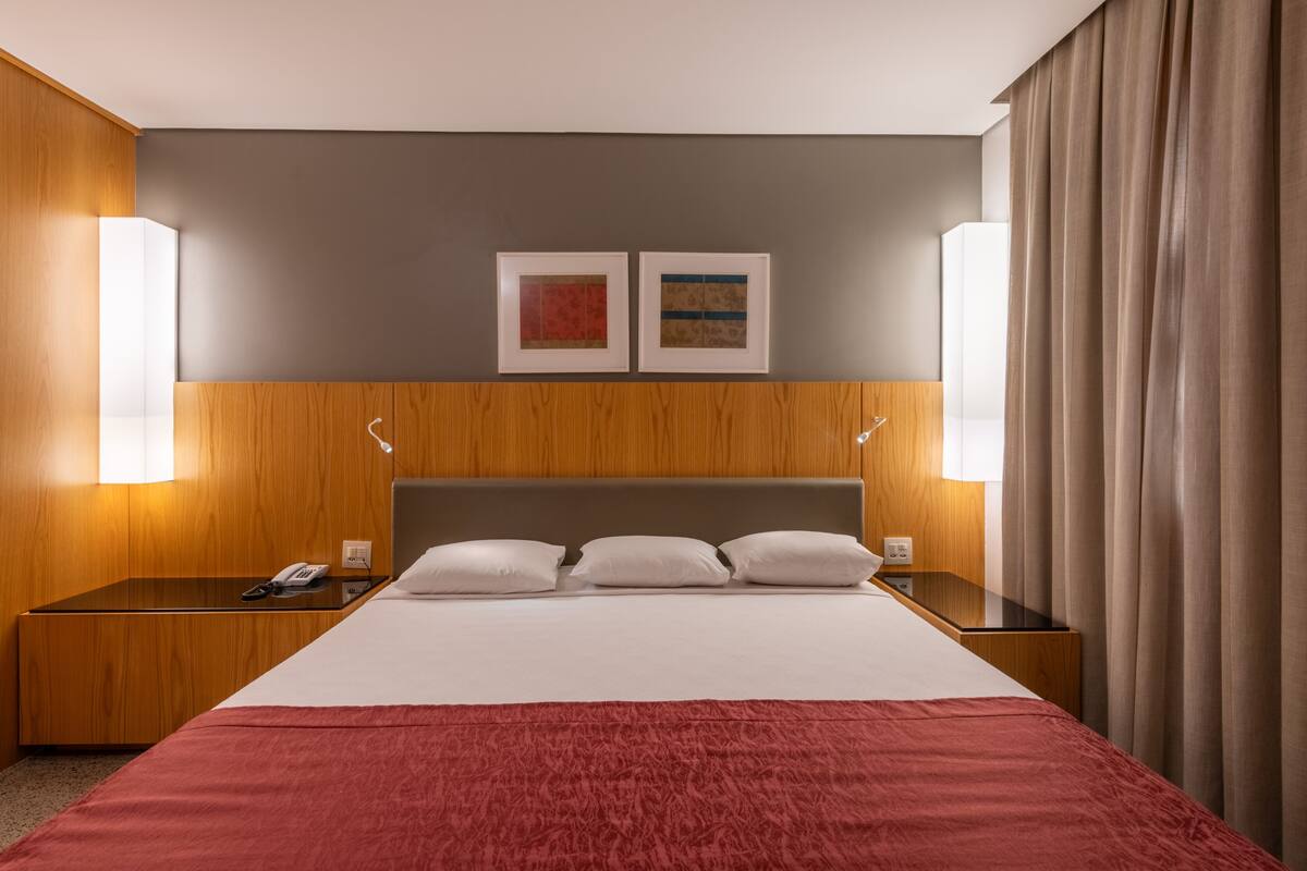 A hotel room with a large bed, wooden headboard, two bedside tables, a telephone, and two framed pictures on the wall.