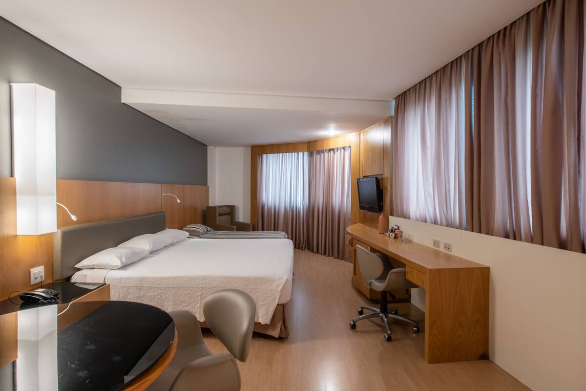 A hotel room with a bed, desk, chair, TV, and curtains.