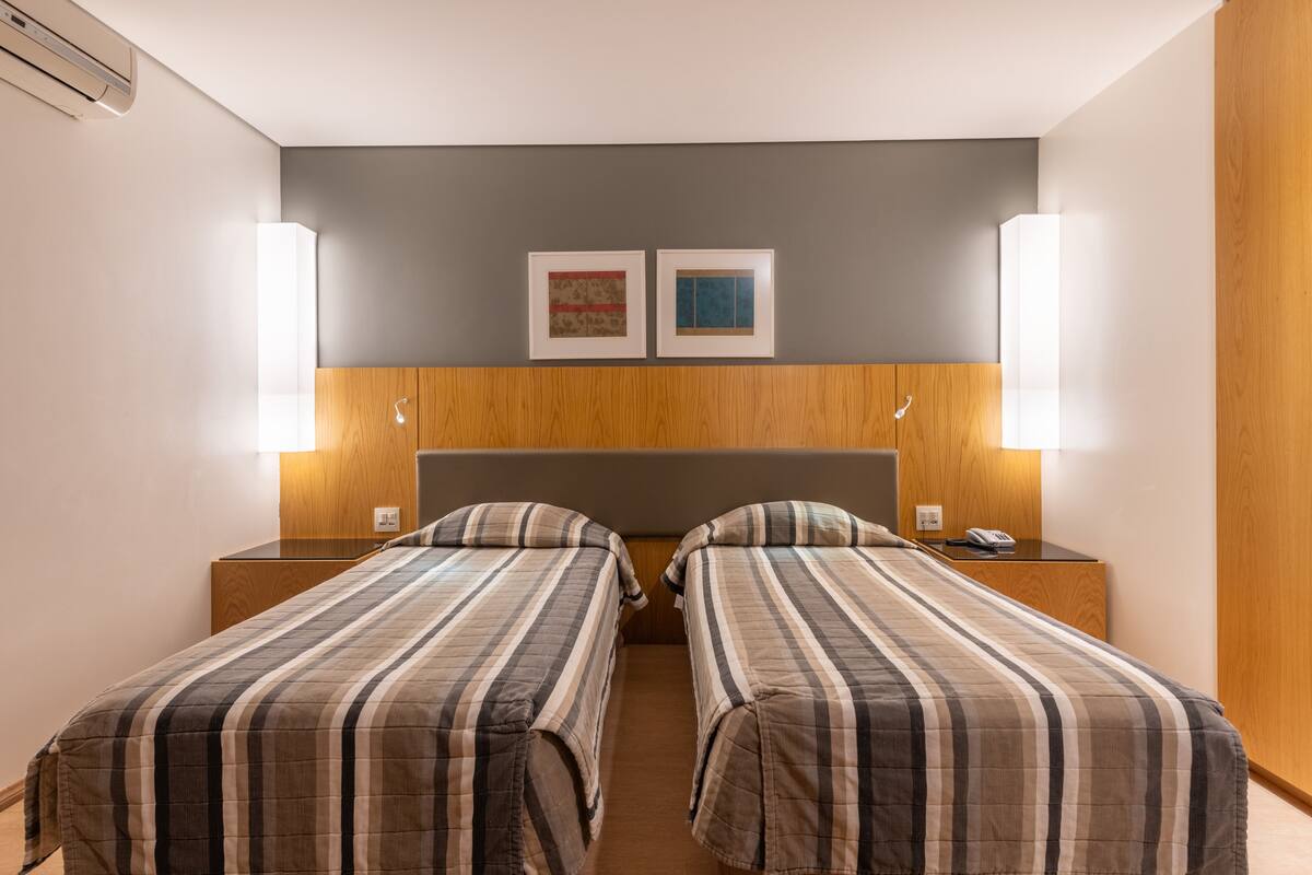 A hotel room with two beds, wooden headboard, wall-mounted artwork, bedside lamps, and a telephone on the nightstand.