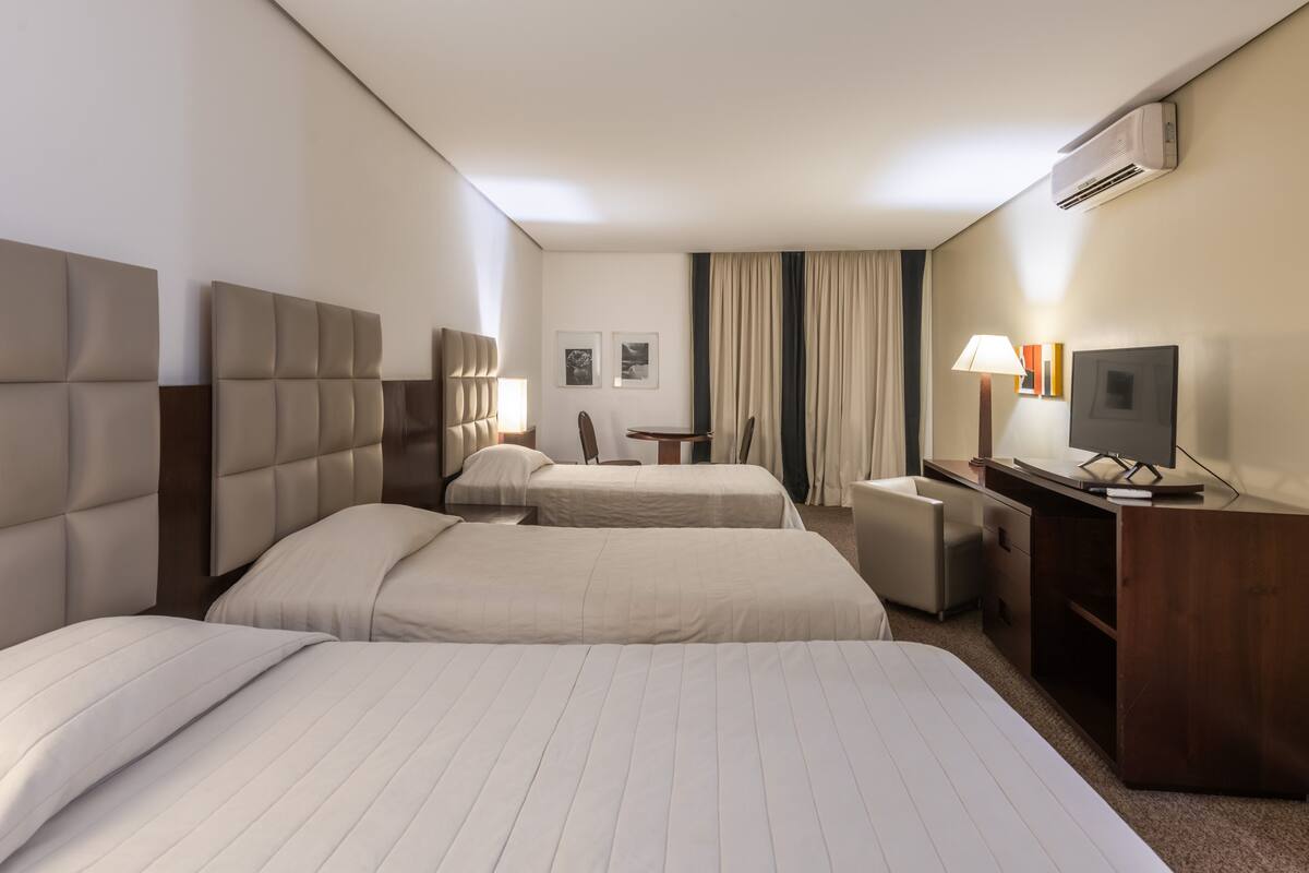 A hotel room with two beds, a desk, a chair, a TV, and an air conditioning unit.