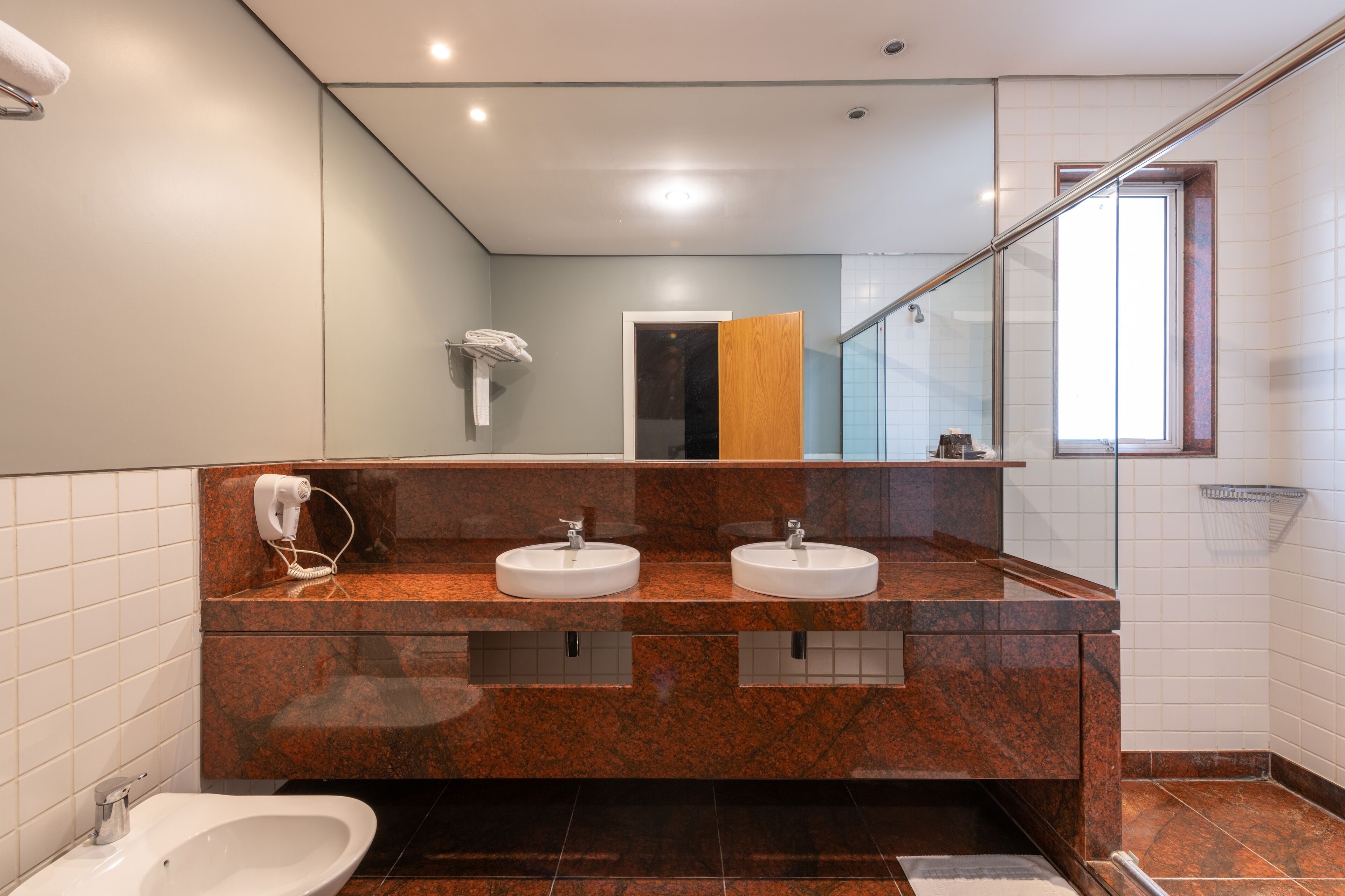 A modern bathroom with two sinks, a bidet, and a glass shower enclosure.