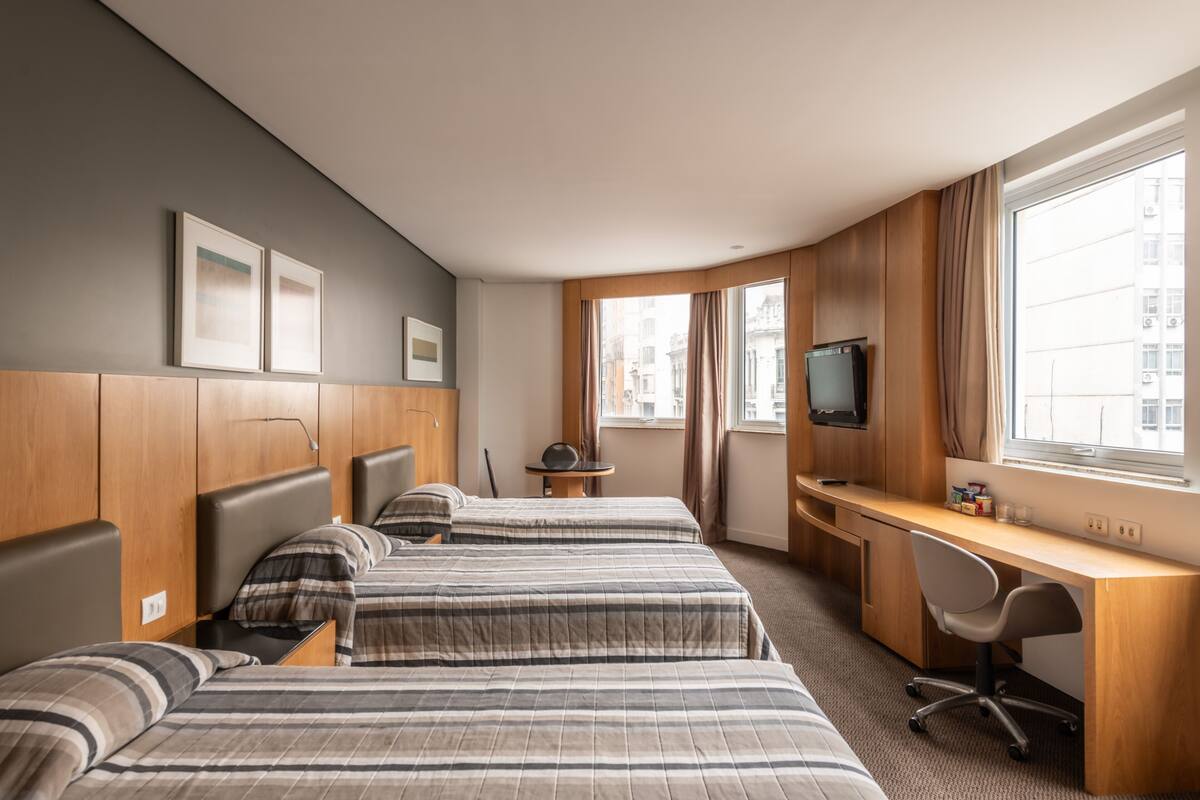 A hotel room with two beds, a desk, a chair, a television, and a window with curtains.