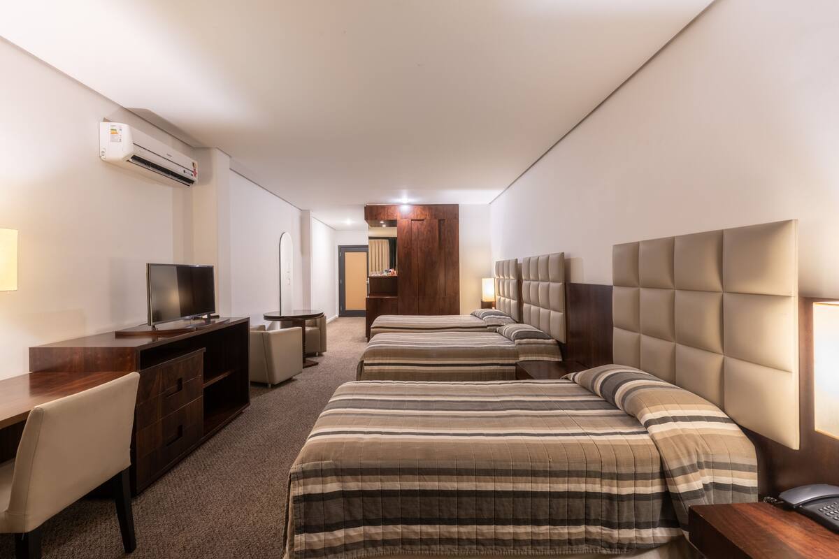 A hotel room with a TV, desk, two beds, and a wooden wardrobe.