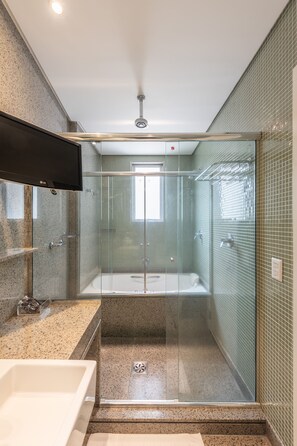 Une salle de bain moderne dotée d’une douche à parois de verre, d’un lavabo intégré et d’un téléviseur à écran plat fixé au-dessus du miroir.