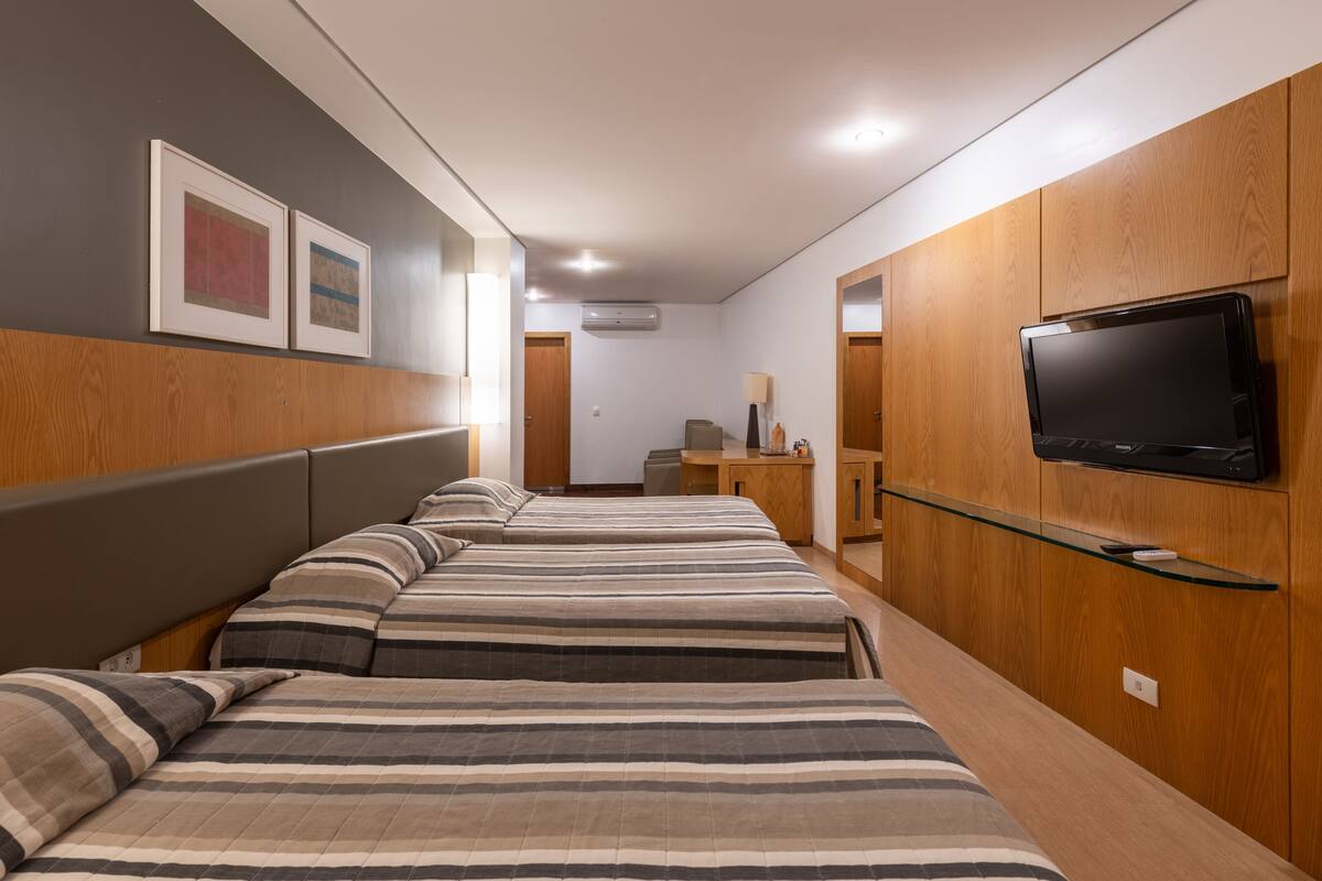 A hotel room with a long bed, a TV mounted on the wall, and wooden paneling.