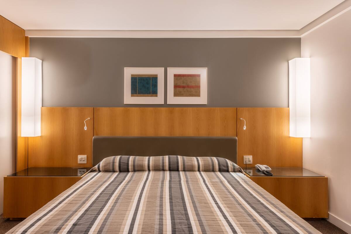 A hotel room with a large bed, wooden headboard, two bedside tables, and wall-mounted lamps.