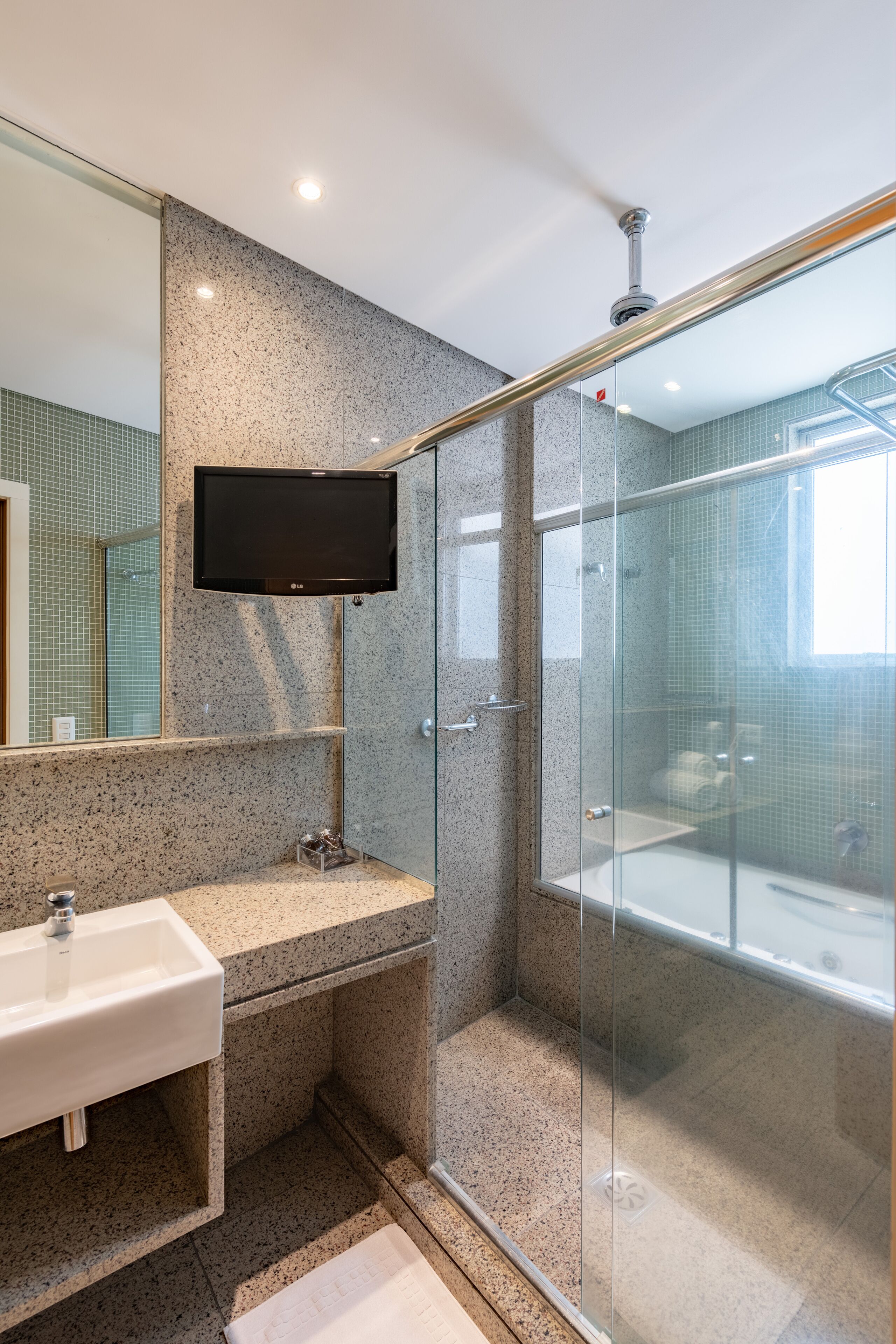 A modern bathroom with a granite countertop sink, a glass shower enclosure, and a mounted television.