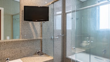 A modern bathroom with a granite countertop sink, a glass shower enclosure, and a mounted television.