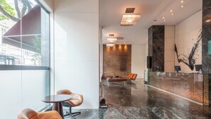 A modern lobby with a glass wall, leather chairs, a brick wall, and a marble floor. - DELPLAZA Marabá São Paulo (São Paulo)