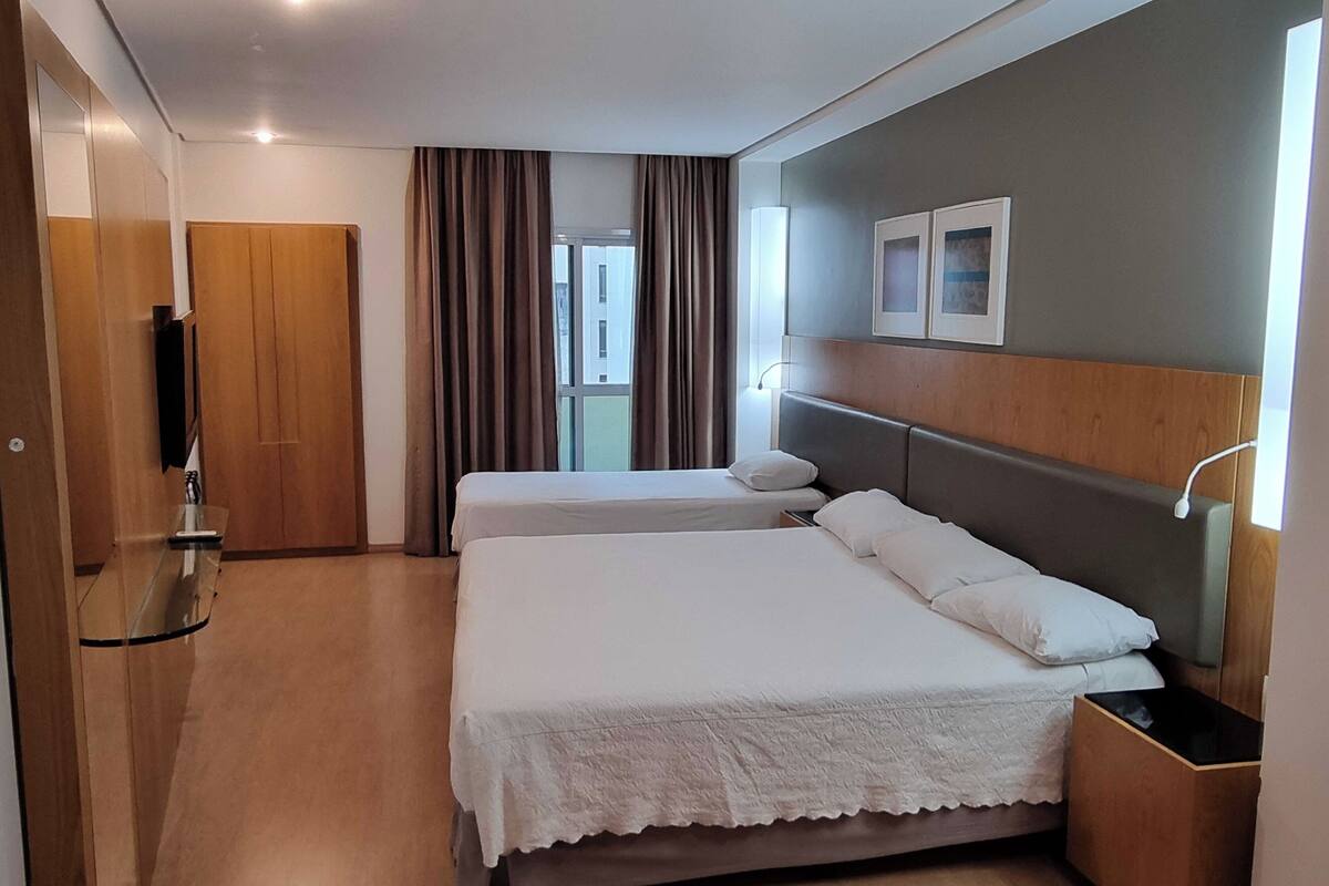 A hotel room with two beds, a wooden wardrobe, a TV, and a window with curtains.
