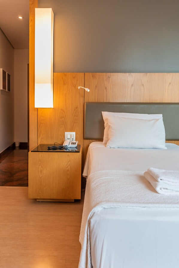 Une chambre d’hôtel avec une tête de lit en bois, une table de chevet avec une lampe, un téléphone et des serviettes soigneusement pliées.