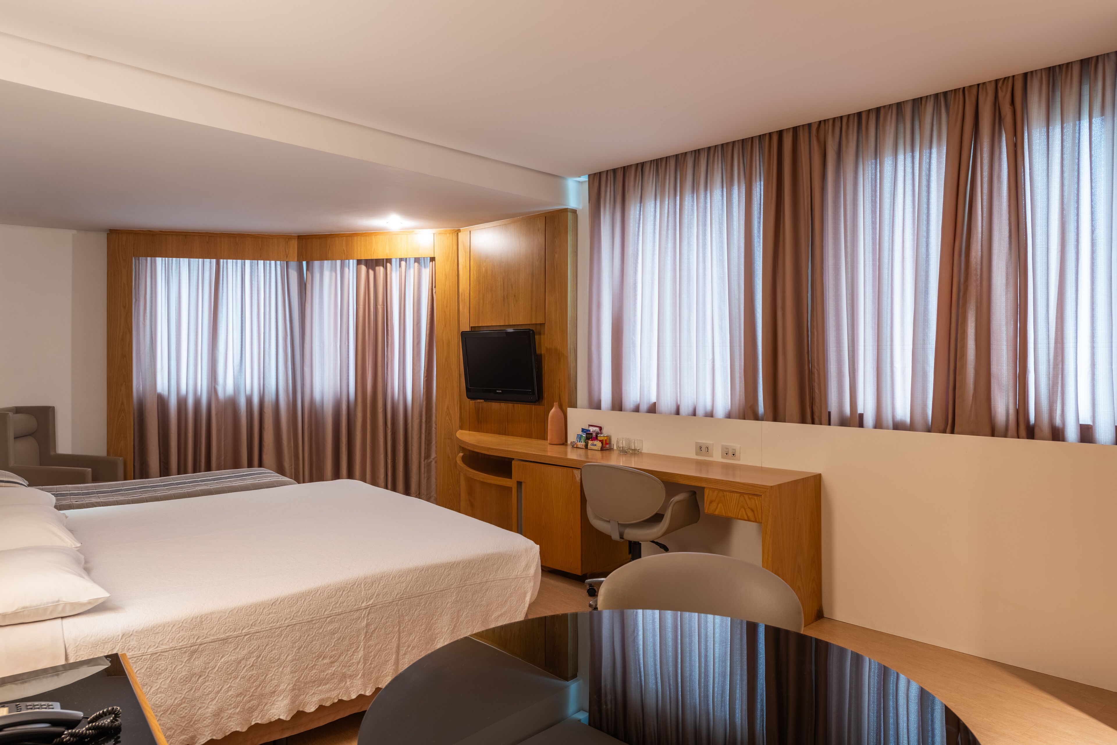 Una habitación de hotel con una cama, un escritorio, una silla, un televisor y cortinas.