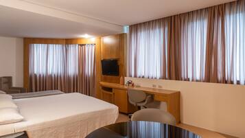 Una habitación de hotel con una cama, un escritorio, una silla, un televisor y cortinas.