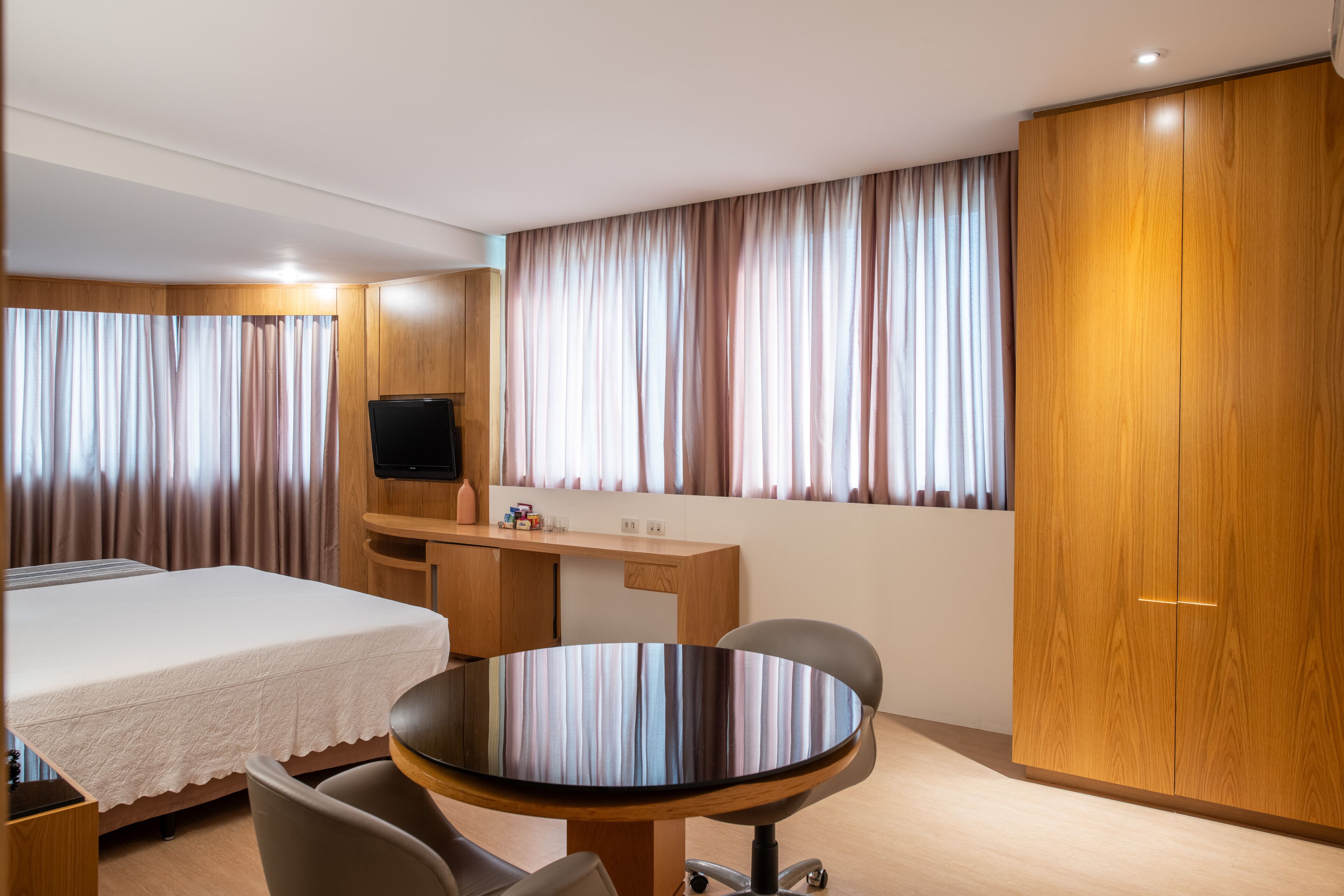Una habitación de hotel con una cama, un escritorio, un televisor y una mesa redonda con sillas.