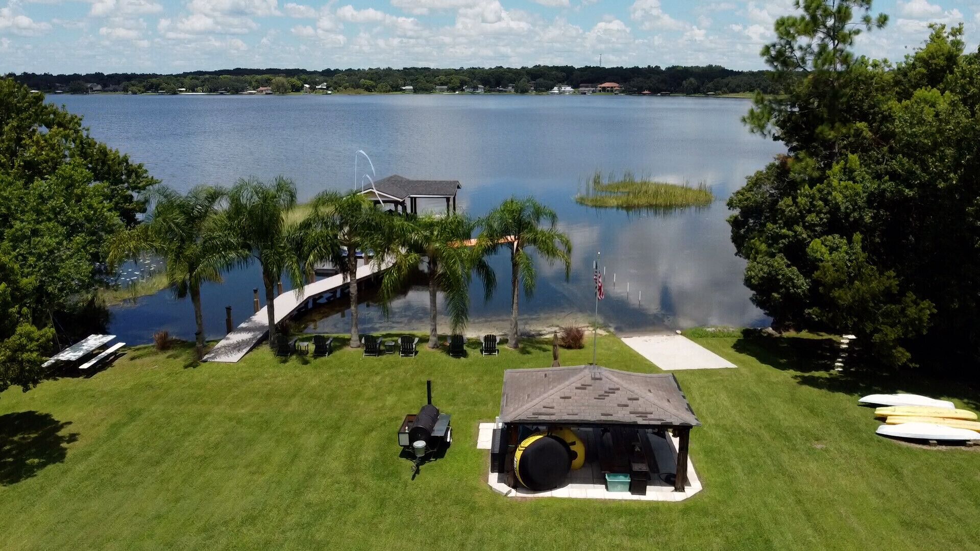 A lakeside property with a dock, lounge chairs, and a small building with a roof.
