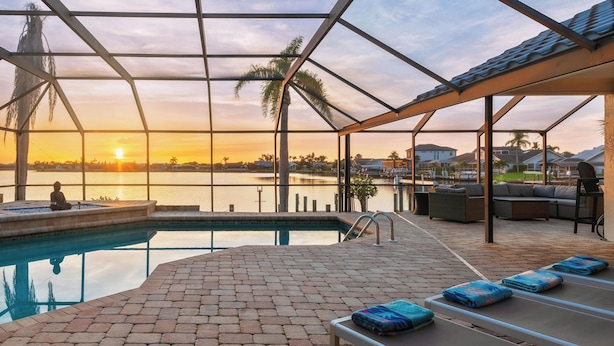 Ein Poolbereich mit Liegestühlen und Blick auf den Sonnenuntergang über dem Wasser.