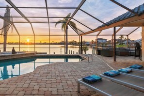 Zona de piscina con sillones de descanso y vista al atardecer sobre el agua.