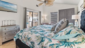 Ein Schlafzimmer mit Bett, Deckenventilator, Kommode und einer Tür zu einem anderen Raum.