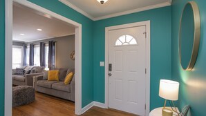 Una sala de estar con pared verde azulada, una puerta blanca y una lámpara sobre una mesita.