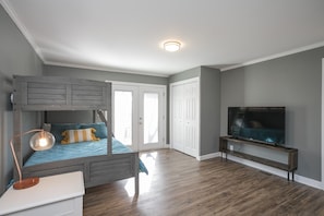 A bedroom with a bunk bed, a desk with a lamp, a TV on a stand, and a wardrobe.