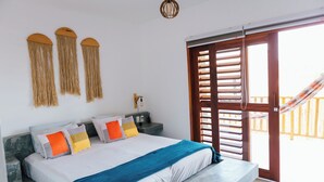 A bedroom with a bed, nightstands, a hanging light fixture, and a view of the outside through a wooden door. - Vila Tuga (Cruz)