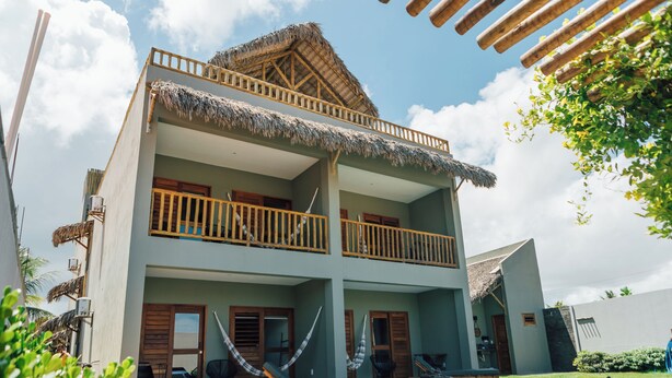 A two-story building with a pool, a thatched roof, and a balcony with wooden railings. - Vila Tuga (Cruz)