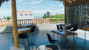 An outdoor dining area with tables and chairs, a thatched roof, and a view of the cityscape. - Vila Tuga (Cruz)