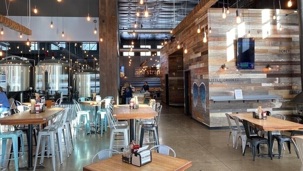 A restaurant interior with high ceilings, exposed ductwork, and hanging pendant lights. Tables are arranged in the center with chairs around them. - Lake View Getaway (Benton Harbor)