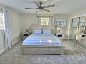 A bedroom with a bed, two bedside tables, a ceiling fan, and a window with curtains.