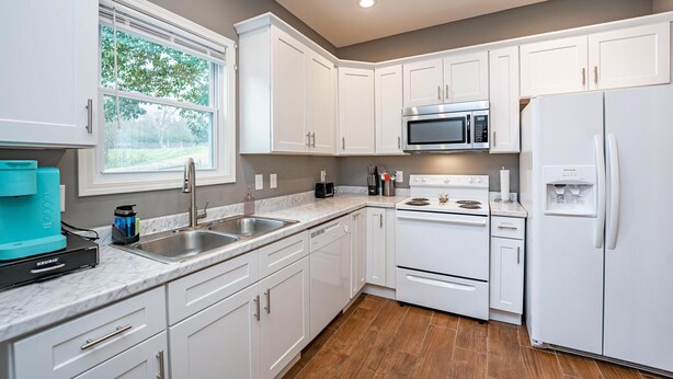 A modern kitchen with white cabinets, a stainless steel sink, a built-in microwave, a stove, and a refrigerator. - Cheerful Pet-Friendly Bungalow 1 Block from Downtown Laurens (Laurens)
