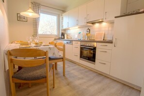 Una cucina moderna con mobili bianchi, forno integrato e zona pranzo con tavolo apparecchiato per due.
