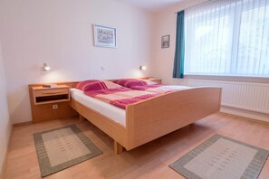 Un dormitorio con cama de madera, mesitas de noche, ventana con cortinas y un radiador.